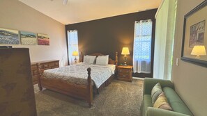 A bedroom with a wooden bed, two bedside tables with lamps, a green armchair, and a dresser.
