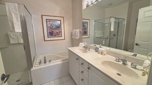 A bathroom with two sinks, a shower, and a large mirror.