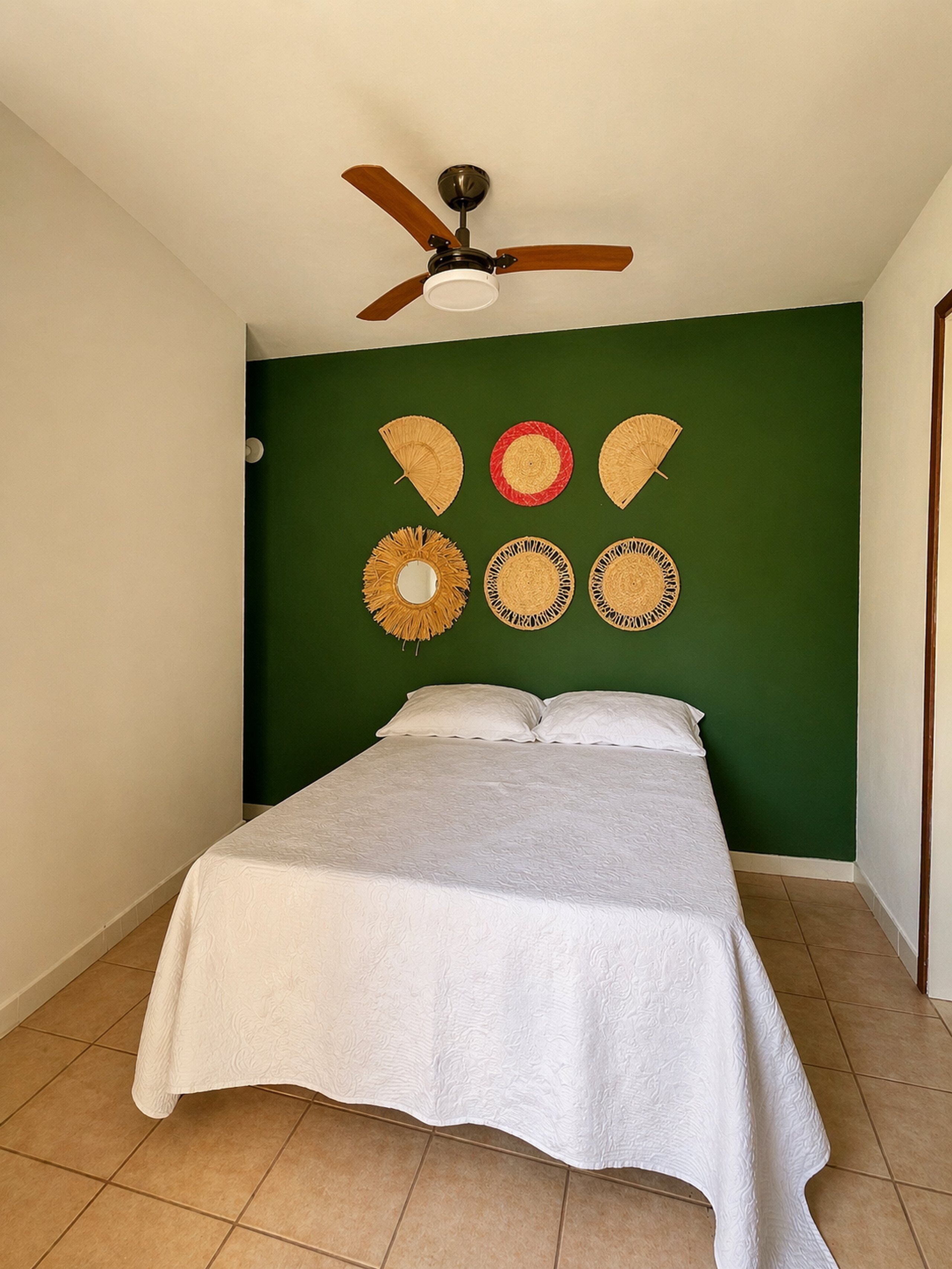 A bedroom with a bed, a ceiling fan, and wall decorations.