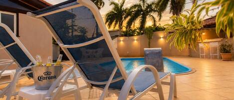Zona de piscina con sillones de descanso, un balde de cerveza Corona y una piscina.
