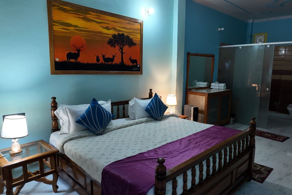 A bedroom with a bed, bedside tables, a nightstand, a dresser, a mirror, and a bathroom visible through an open door.