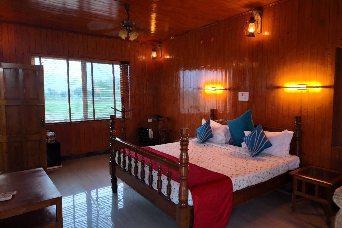 A wooden room with a bed, a chair, a table, and a window with blinds.