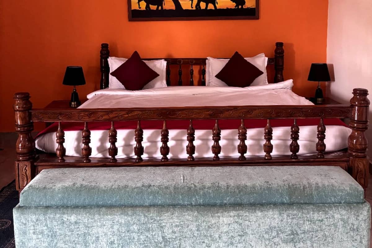 A bedroom with a wooden bed, two bedside tables with lamps, a large painting of elephants, and a ceiling fan.