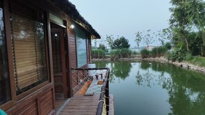 Une maison en bois dotée d’un porche donnant sur une étendue d’eau paisible, le tout entouré de verdure.