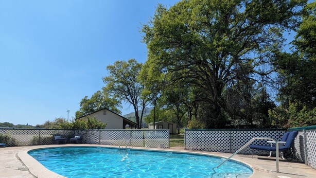 A swimming pool with a white lattice fence, a concrete deck, and a small building in the background. - Squaw Valley Motel Room #1 (Yokuts Valley)