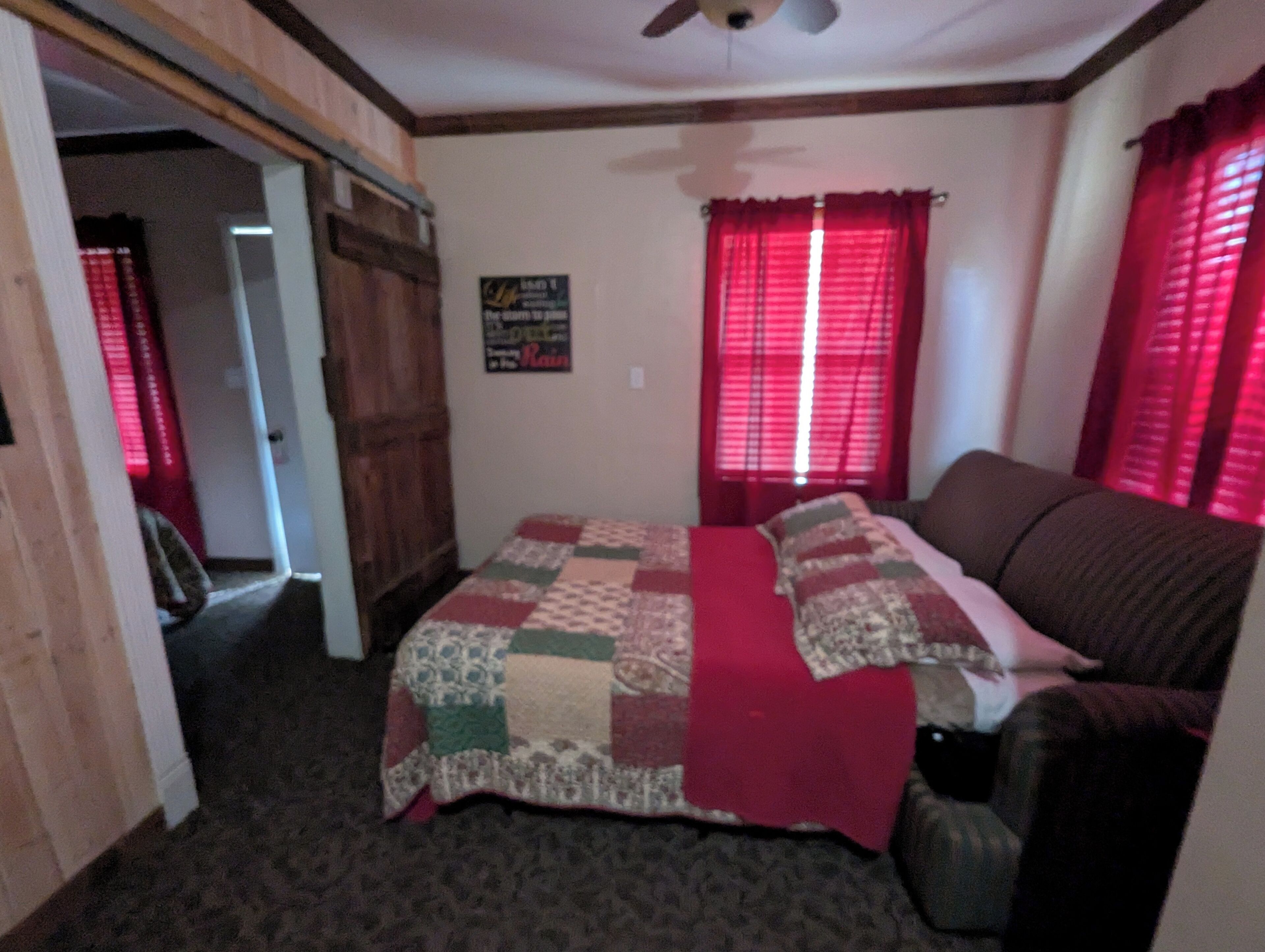 A bedroom with a bed, a wooden wardrobe, a red curtain, and a ceiling fan.