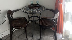 A corner room with a round table, two chairs, a wall-mounted TV, and a sunset painting.