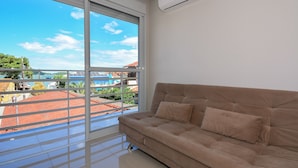 Ein Zimmer mit einer großen Schiebeglasdoor zum Balkon, einem beigen Sofa und einer Klimaanlage an der Wand.