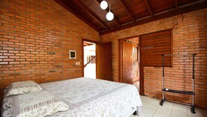 Ein Schlafzimmer mit Backsteinwand, Holzbalkendecke, einem Bett mit Blumenmuster-Bettwäsche und einem Metallregal an der Wand.