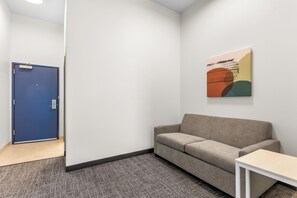 A room with a blue door, a beige sofa, a small white table, and a colorful abstract painting on the wall. - Spark by Hilton Dothan (Dothan)