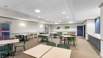 A conference room with multiple tables and chairs, a white ceiling with recessed lighting, and a view of the outdoors through a window.