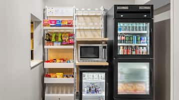 Un angolo cottura compatto con forno a microonde, mini-frigo e dispensa fornita di snack e bevande.