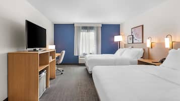 Habitación de hotel con televisor, escritorio, dos camas, una silla y ventana con cortinas.