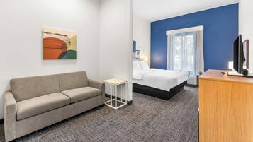 Una habitación de hotel con sofá, una mesita, cama, escritorio y televisor.