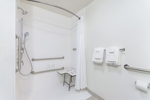 A modern bathroom with a walk-in shower, grab bars, a small table, and a towel rack. - Spark by Hilton Dothan (Dothan)
