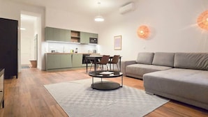 Una sala de estar moderna con un sofá gris, una mesa de comedor con sillas y una cocina con armarios verdes.