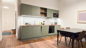 Una cocina compacta con gabinetes verdes, un microondas y una zona de comedor con una mesa y sillas.
