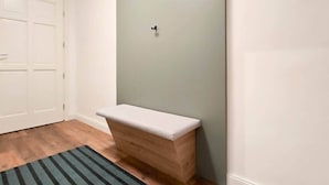 Un pasillo con una puerta blanca, un banco y una lámpara de pared.