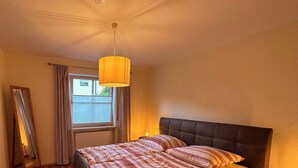 A bedroom with a bed, a bedside table, a mirror, a window with curtains, and a ceiling light. - Vacation apartment with terrace and garden (Piding)