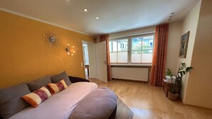 A bedroom with a bed, a wall clock, a radiator, and a window with curtains. - Vacation apartment with terrace and garden (Piding)
