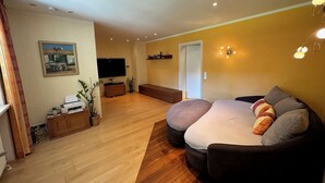 A living room with a wooden floor, a sofa, a TV, and a painting on the wall. - Vacation apartment with terrace and garden (Piding)