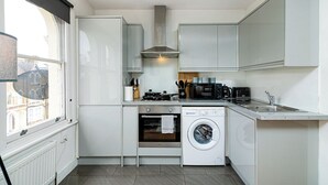 A compact kitchen with white cabinets, a built-in oven, a washing machine, and a coffee maker.