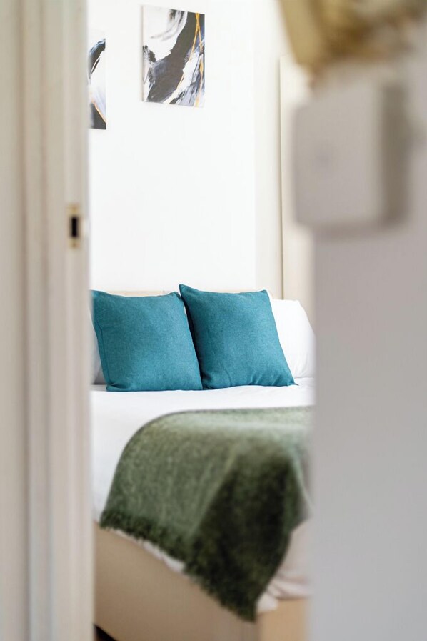 Une chambre à coucher avec un lit, des coussins turquoise et une couverture verte.