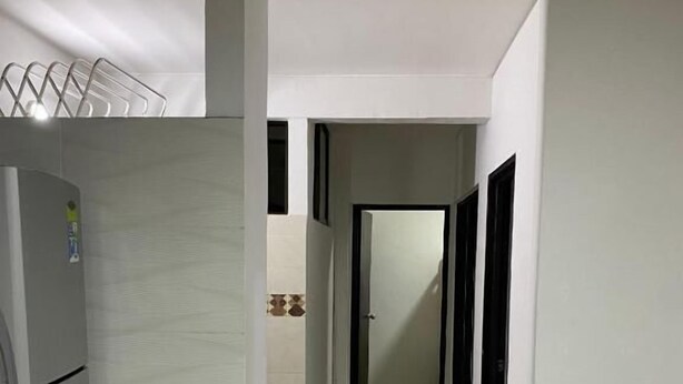 Un pasillo estrecho con un refrigerador a la izquierda, una puerta al final y piso de baldosas.