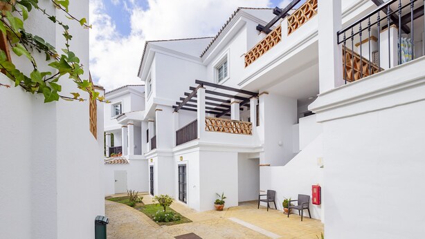 Un edificio blanco con un patio empedrado, una escalera de madera y un pequeño jardín con flores.