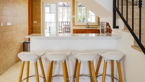 Una cocina moderna con una isla central, taburetes de madera y una escalera con barandilla negra.