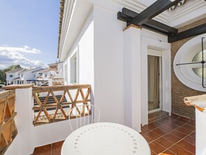 Ein Balkon mit weißem Tisch und Stühlen, einem Holzzimmer und Blick auf benachbarte Häuser.