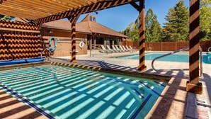 A pool area with a wooden pergola, lounge chairs, and a building with a brick facade. - Steps to Ski*Sleeps 8*Hot Tub* (Park City)