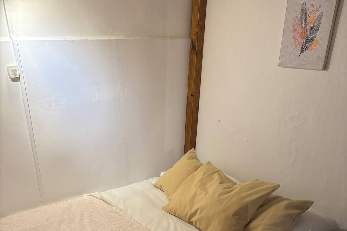 Ein ordentlich gemachtes Bett mit einer beigen Decke und zwei Kissen, ein Holzbalken an der Wand und ein kleines Wandbild.