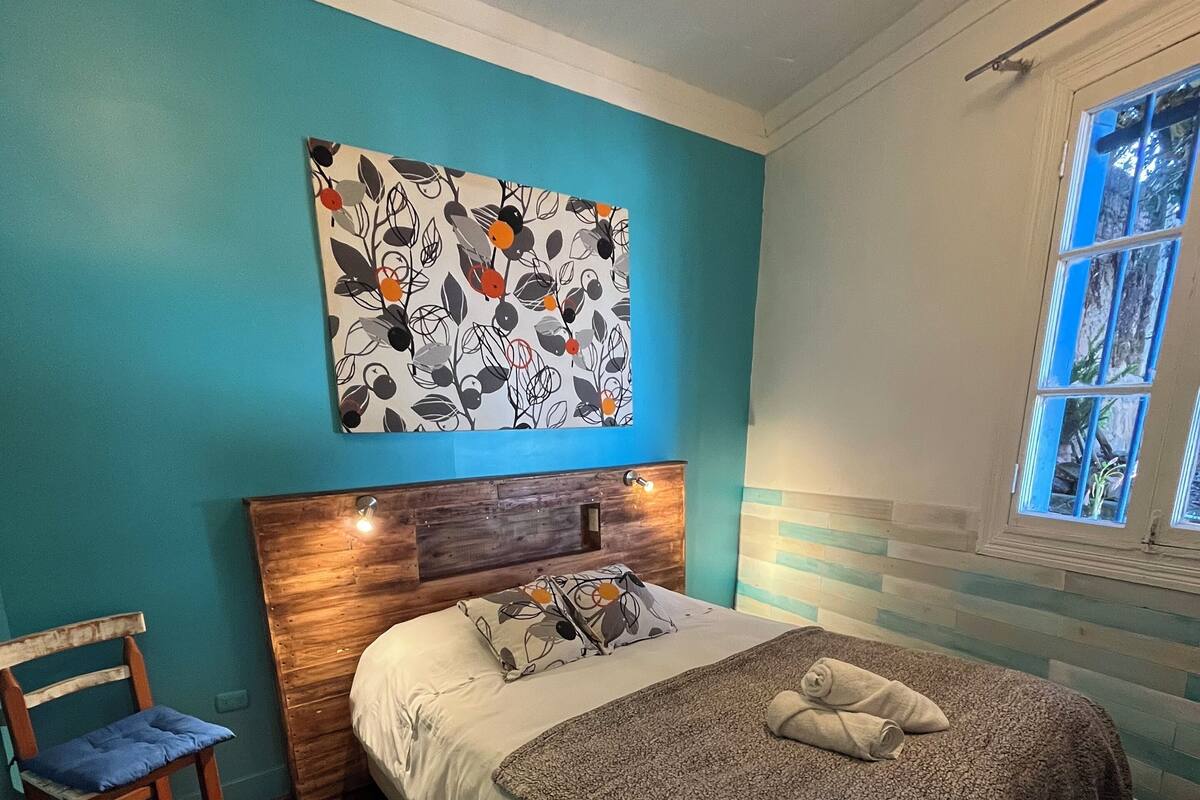 Ein Schlafzimmer mit Bett, Stuhl, Fenster und einem Wandbild.