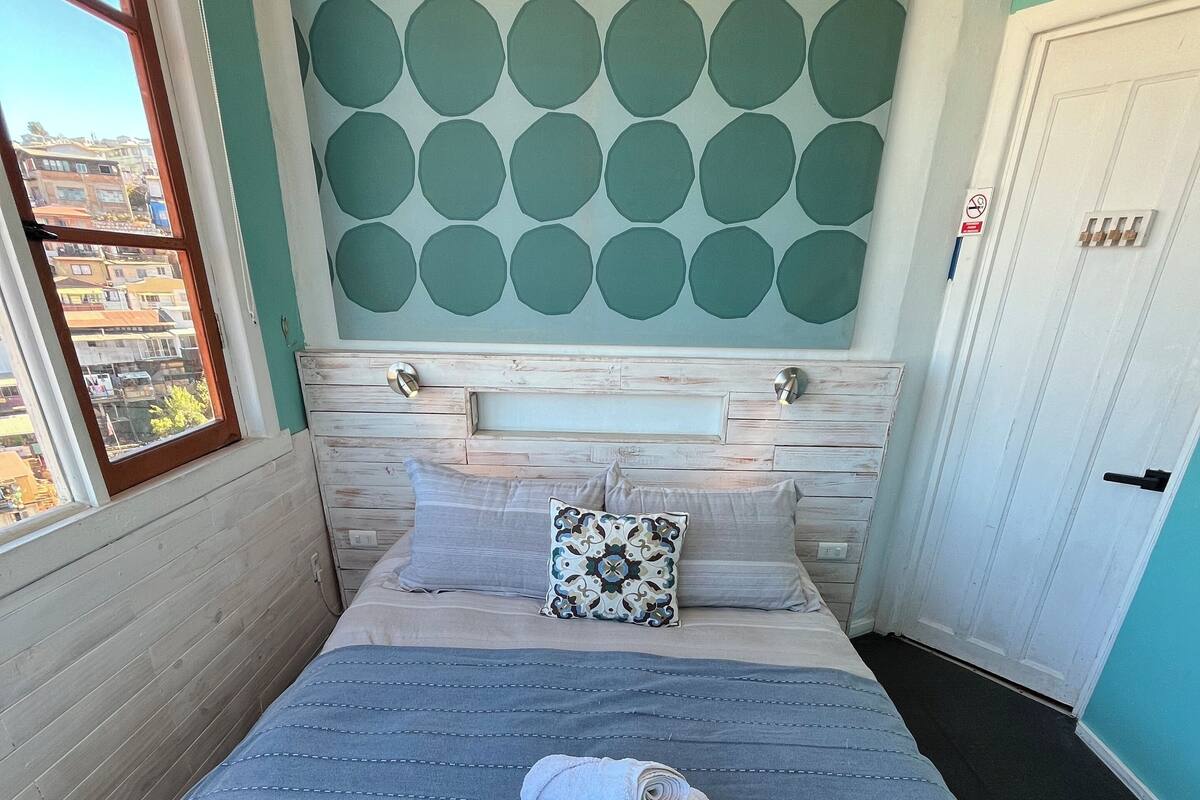 Ein ordentlich bezogenes Bett mit blauer Bettdecke, einem Kissen und einem zusammengerollten Handtuch.