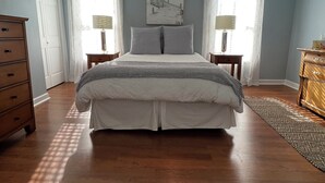 Un dormitorio con cama, ventilador de techo, dos mesitas de noche con lámparas, cómoda y un cuadro en la pared.