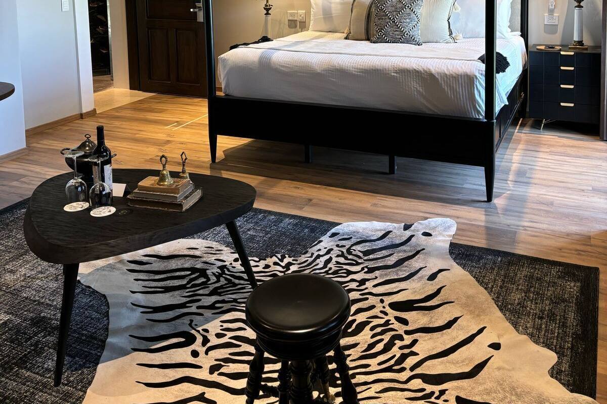 A four-poster bed with a dark frame, a round coffee table with decorative items, and a zebra-print rug.