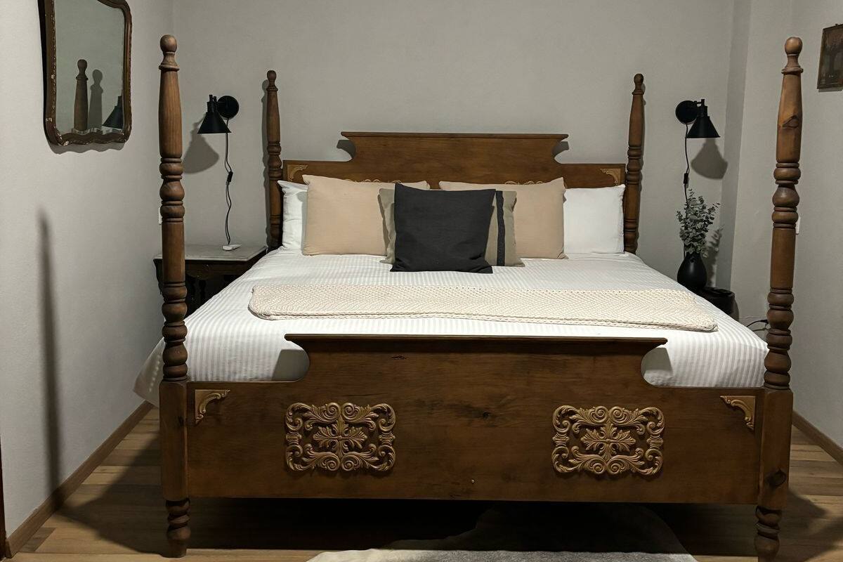 A four-poster bed with a wooden headboard and footboard, a white bedspread, and a gray fur rug on the floor.