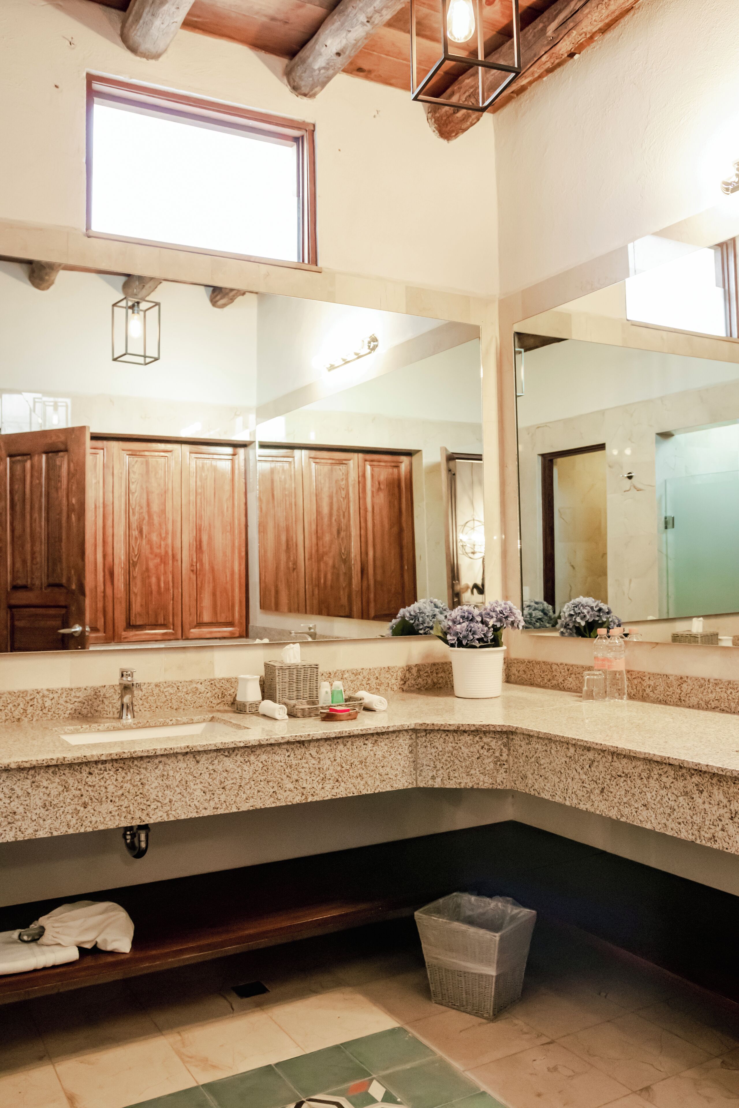 A bathroom with wooden cabinets, a granite countertop, a sink, a mirror, and a potted plant.