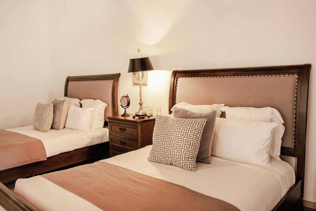 A hotel room with two beds, each with a wooden headboard, a nightstand with a lamp, and a mirror.