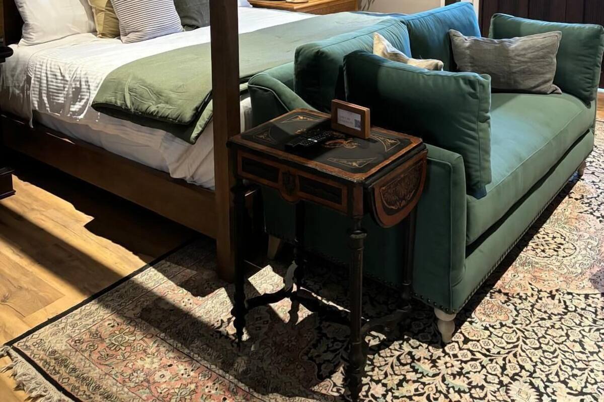 A four-poster bed with a green upholstered sofa and a small side table.