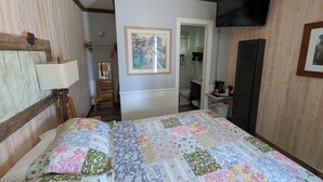 A bedroom with a large bed, a bedside table with a lamp, a framed picture on the wall, and a television mounted on the wall. - Squaw Valley Motel Room #2 (Yokuts Valley)