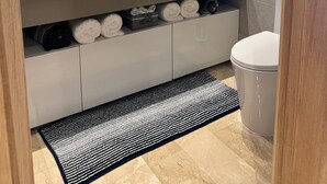 Ett modernt badrum med en stor spegel, ett handfat och en toalett. Handdukar och hygienartiklar finns på bänkskivan.