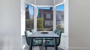 A corner room with a bay window, a dining table with chairs, and a view of neighboring houses.