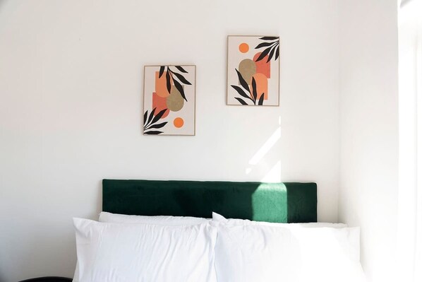 A bed with a green headboard, white pillows, and two abstract wall art pieces.