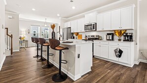 Une cuisine moderne avec des meubles blancs, un îlot central doté de tabourets, des appareils en acier inoxydable et un plancher en bois.