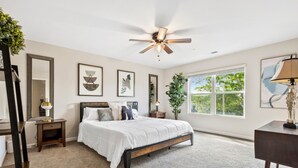 Une chambre à coucher avec un lit, un ventilateur de plafond, une fenêtre et une plante.