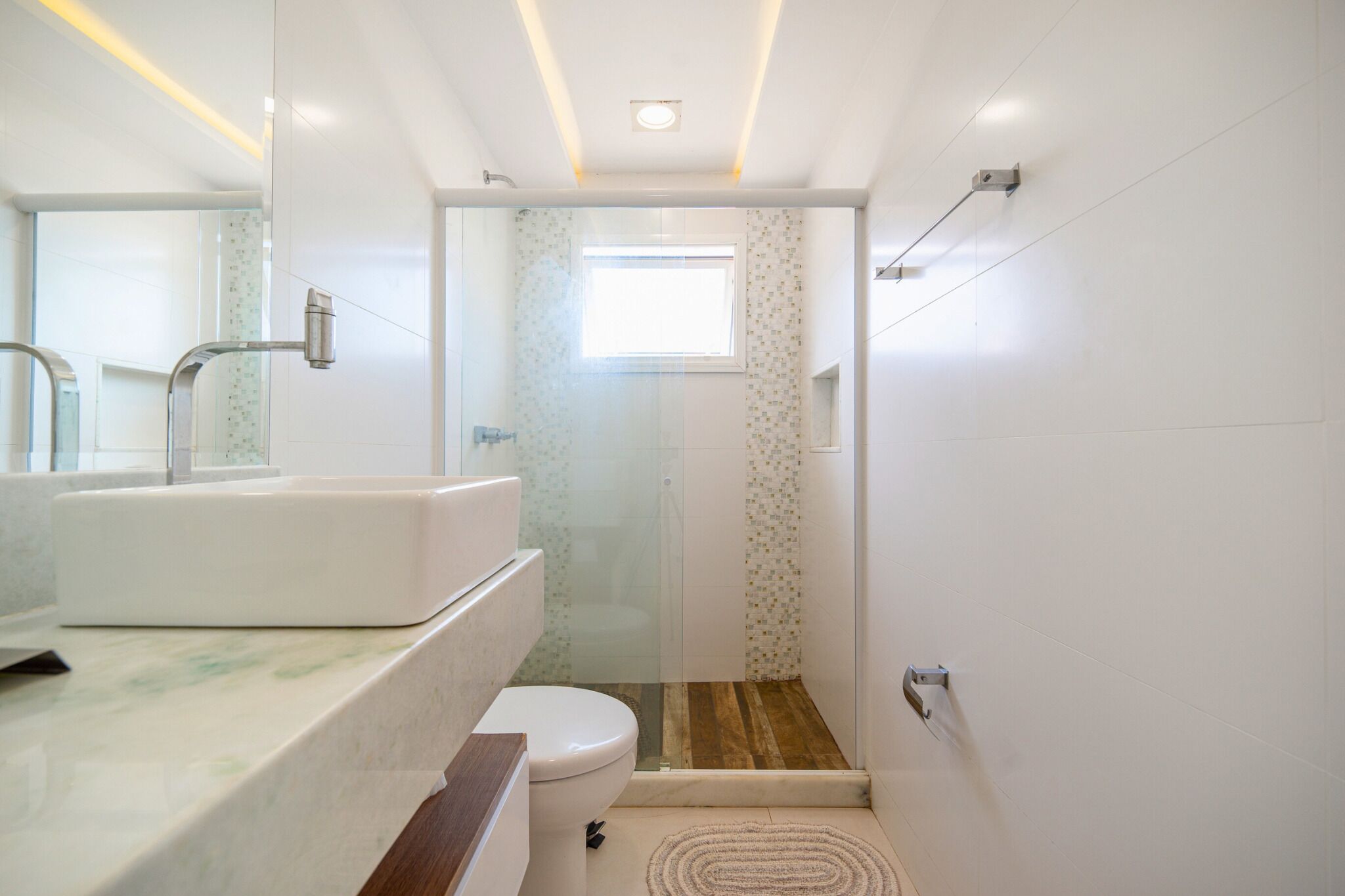 A modern bathroom with a glass shower enclosure, a white sink, and a wooden floor.