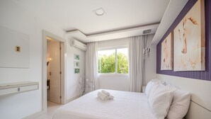 A hotel room with a large bed, a window with curtains, a wall-mounted air conditioner, and a door leading to another room. - Bz68 Centro Casa piscina priv 6 quartos (Buzios)
