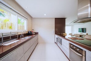 A modern kitchen with a large window, stainless steel appliances, and a clean, tiled floor. - Bz68 Centro Casa piscina priv 6 quartos (Buzios)